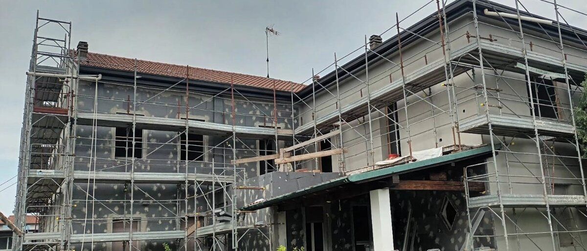 Palazzina residenziale con ponteggio montato su tutti i lati, pannelli isolanti in corso di posa.