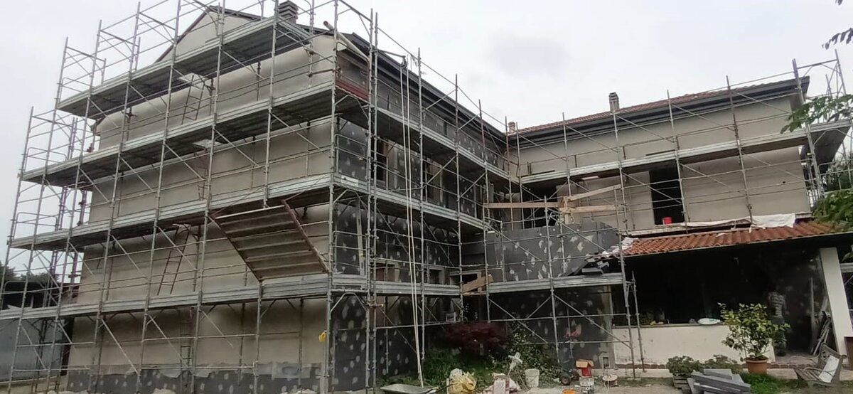 Edificio residenziale interamente ponteggiato: su una parte della facciata i pannelli isolanti sono gia' tassellati, sull'altra la rasatura e' finita.